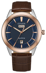 Gents Citizen Watch AW0096-06L. This Corso model is shown in a two-tone rose gold-tone and white stainless steel case, brown leather band, and a navy blue dial with a day and date window. Features include: Eco-Drive technology, sapphire crystal, and water resistance up to 100 meters. 